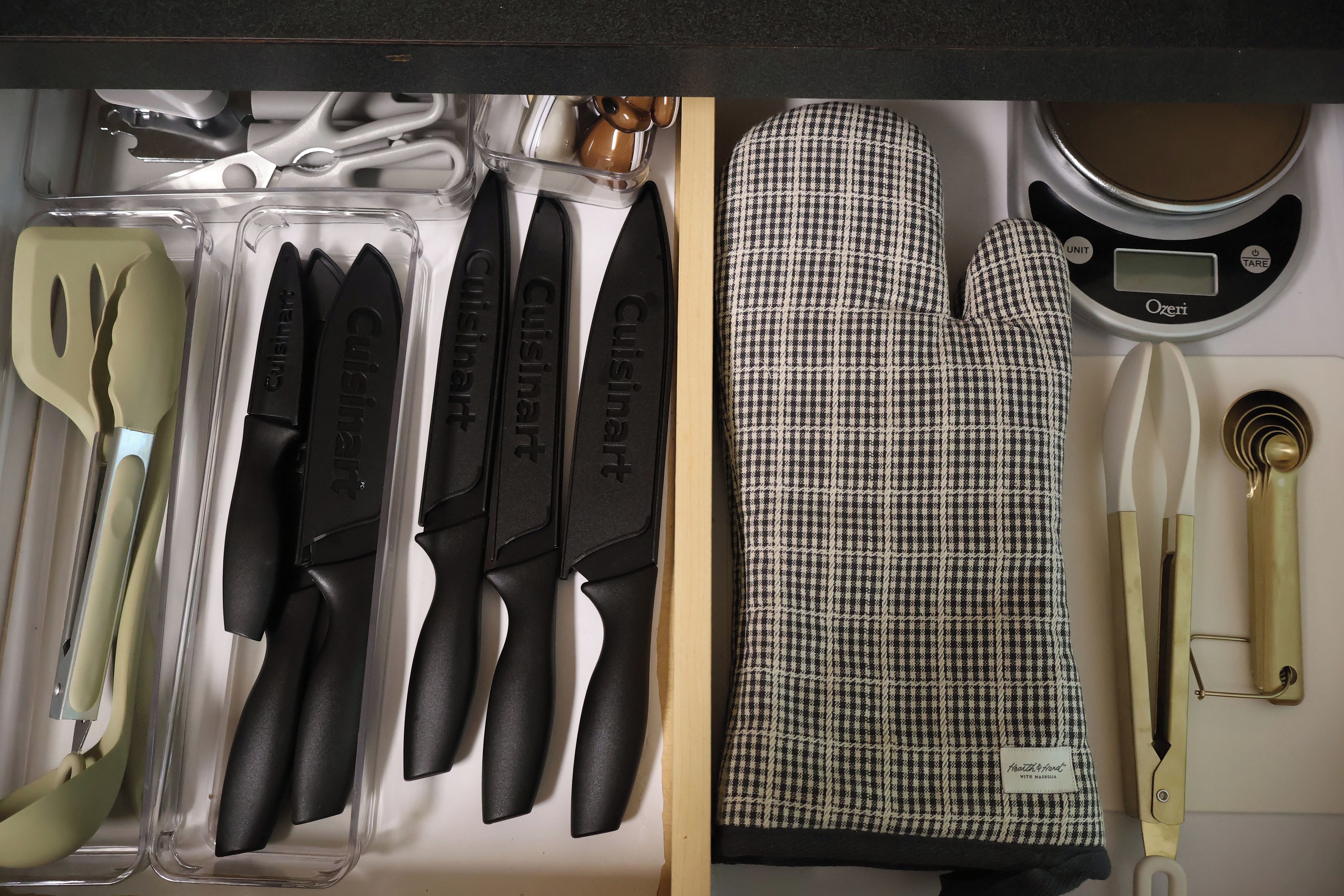 Un cajón de cocina con diversos utensilios, incluyendo cuchillos, una espátula y una taza medidora.