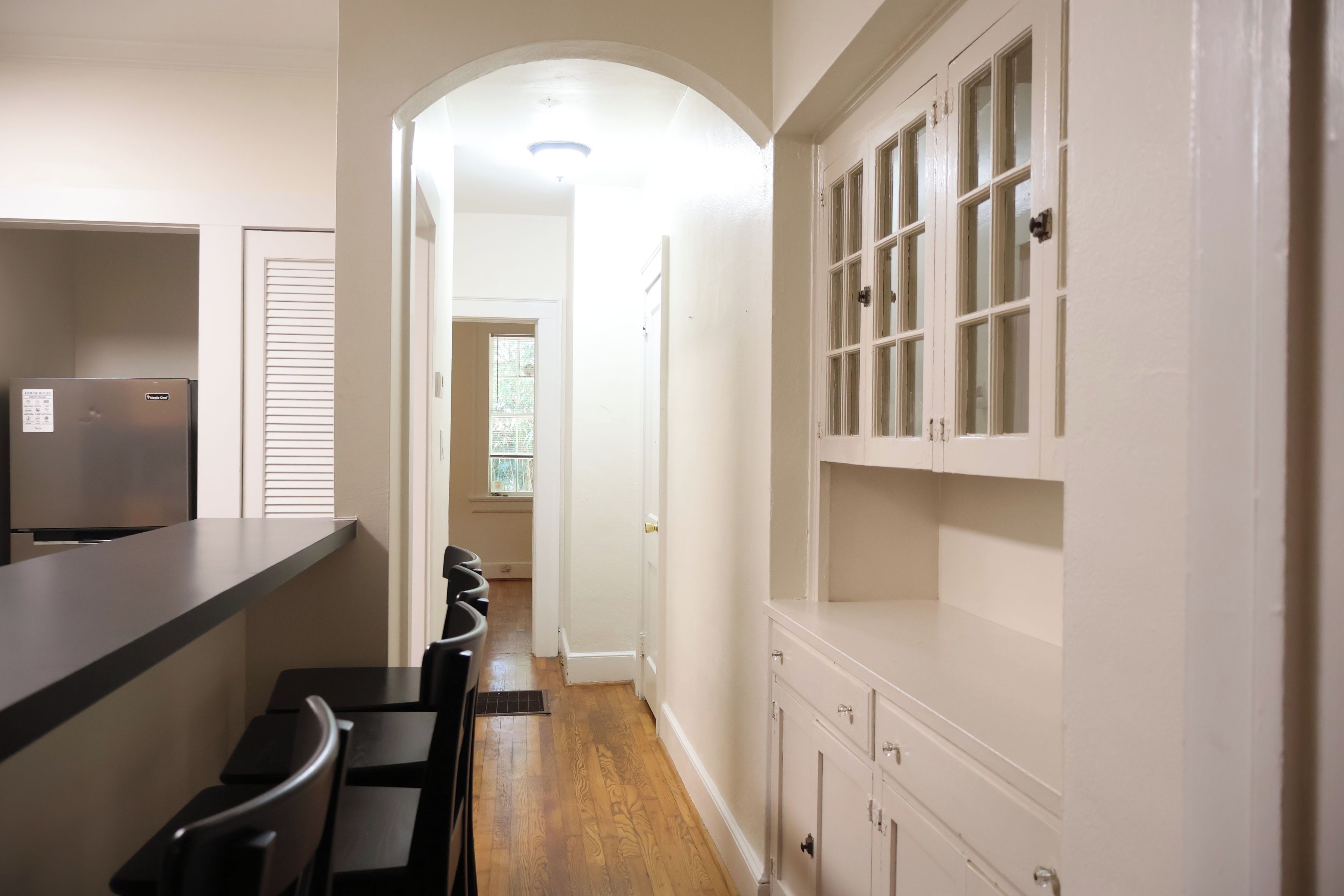 A kitchen with a refrigerator, a dining table with chairs, and a hallway leading to a door.