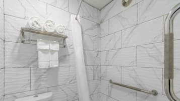 A bathroom with white marble tiles, a shower with a white curtain, a towel rack with rolled towels, and a handrail.