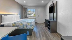 Habitación de hotel con cama, escritorio, silla, televisor y ventana.