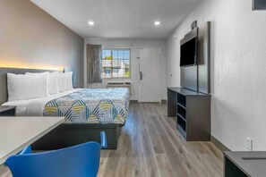 Habitación de hotel con cama, escritorio, silla, televisor y ventana.