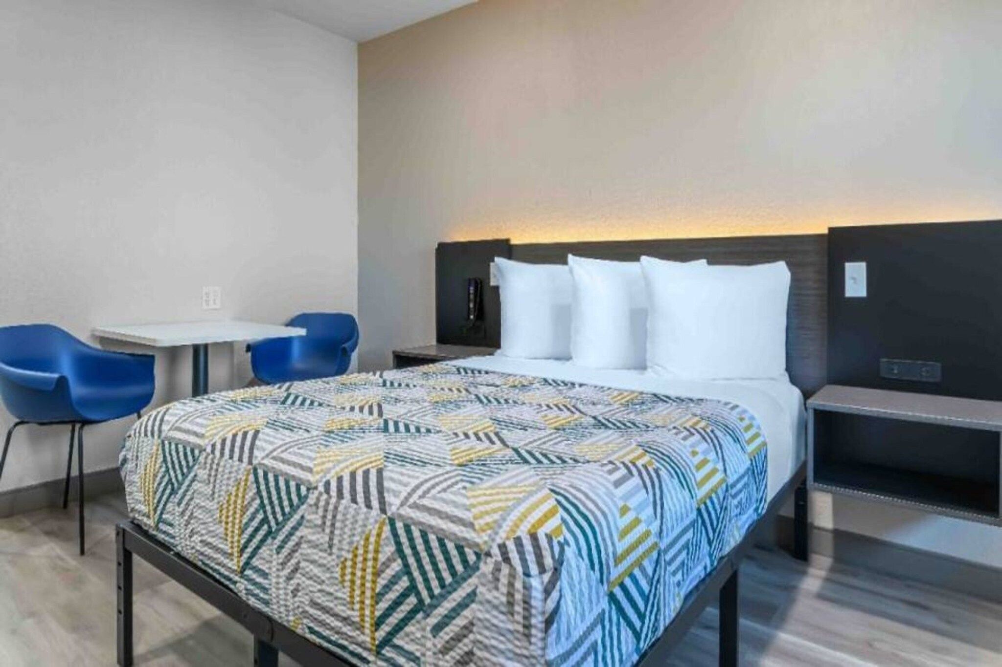 A hotel room with a bed, a desk, a chair, and a nightstand.