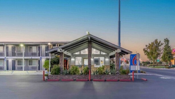 Un motel con entrada cubierta, estacionamiento y un letrero con el número '6' que indica la ubicación.