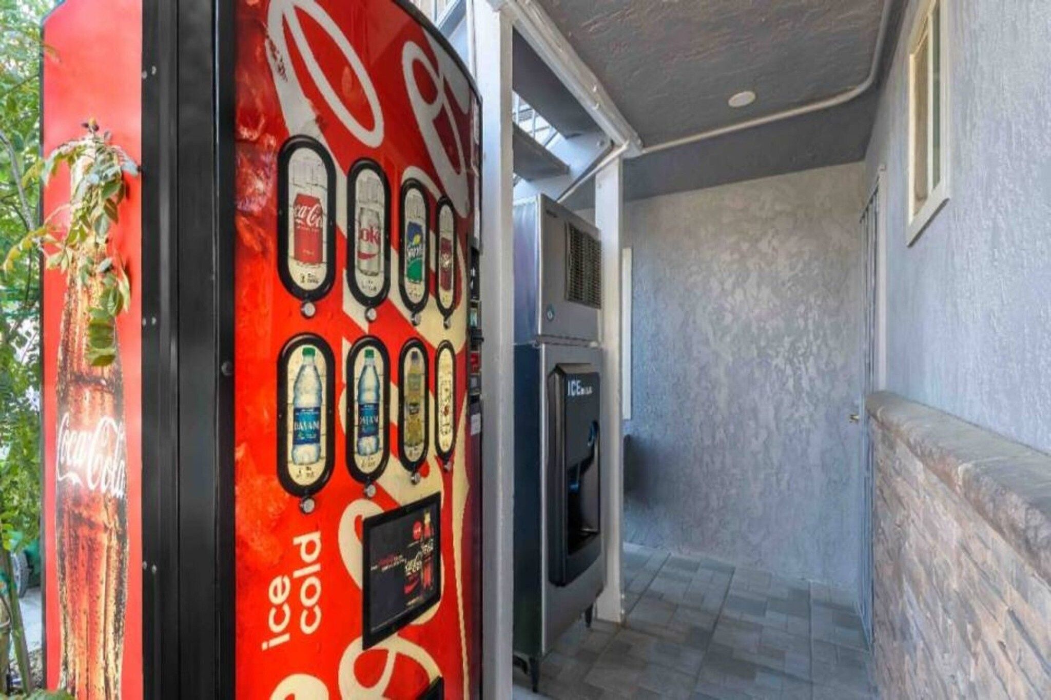 A vending machine with various beverage options, a refrigerator, and a staircase leading to an upper level.