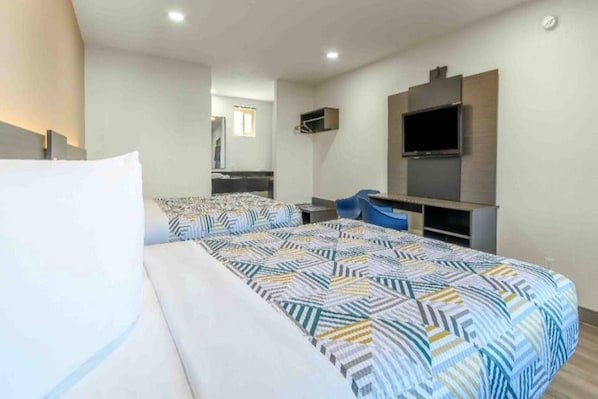 A hotel room with a large bed, a desk, a chair, a TV, and a mirror.