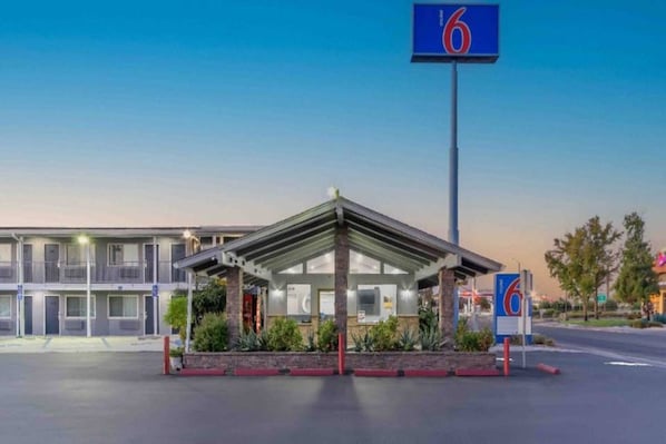 Un motel con entrada cubierta, estacionamiento y un letrero con el número '6' que indica la ubicación.