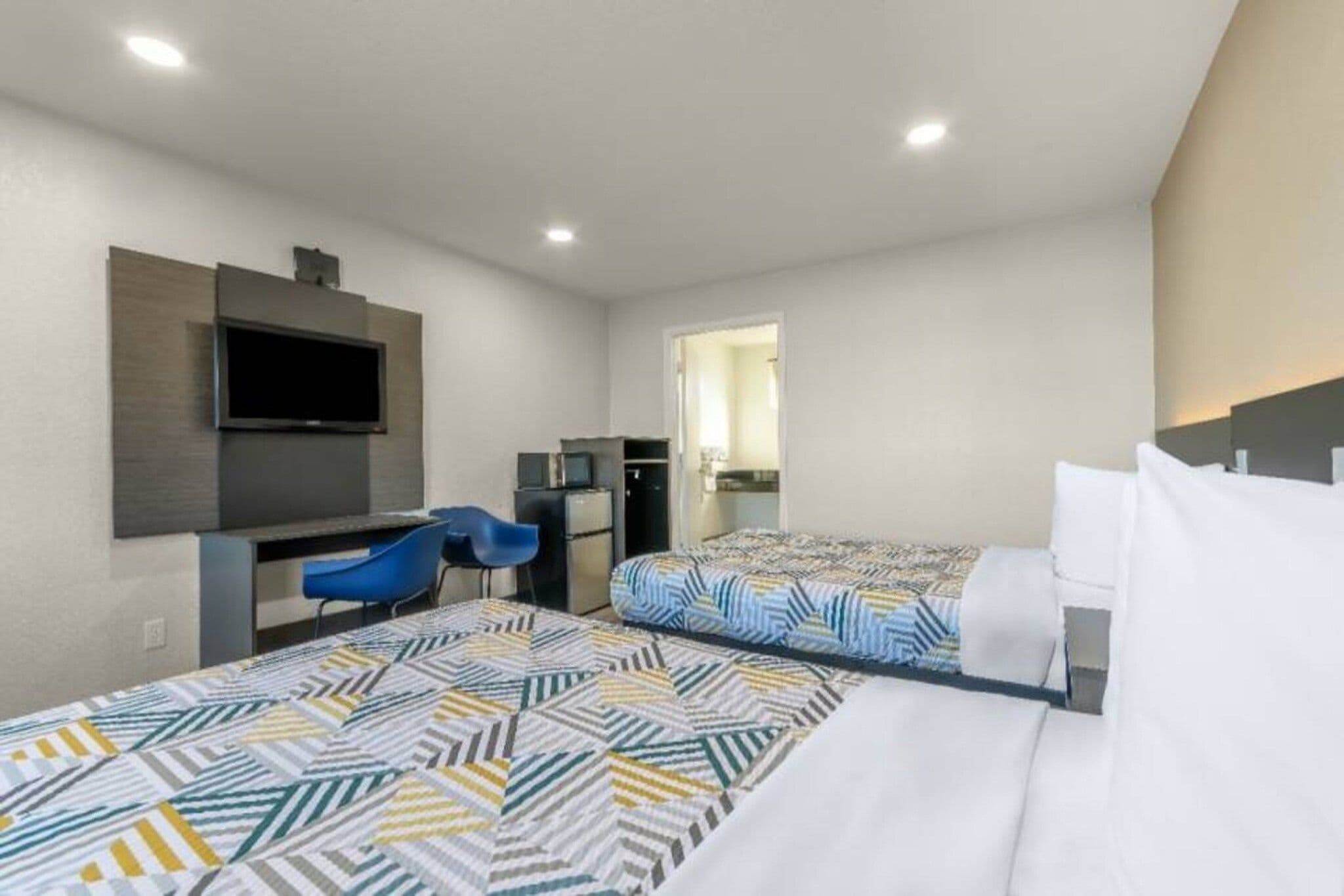 A hotel room with two beds, a desk, a chair, a TV, and a mirror.