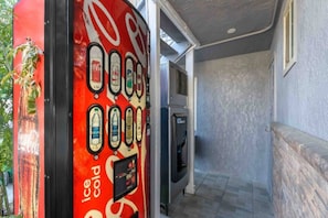 A vending machine with various beverage options, a refrigerator, and a staircase leading to an upper level.