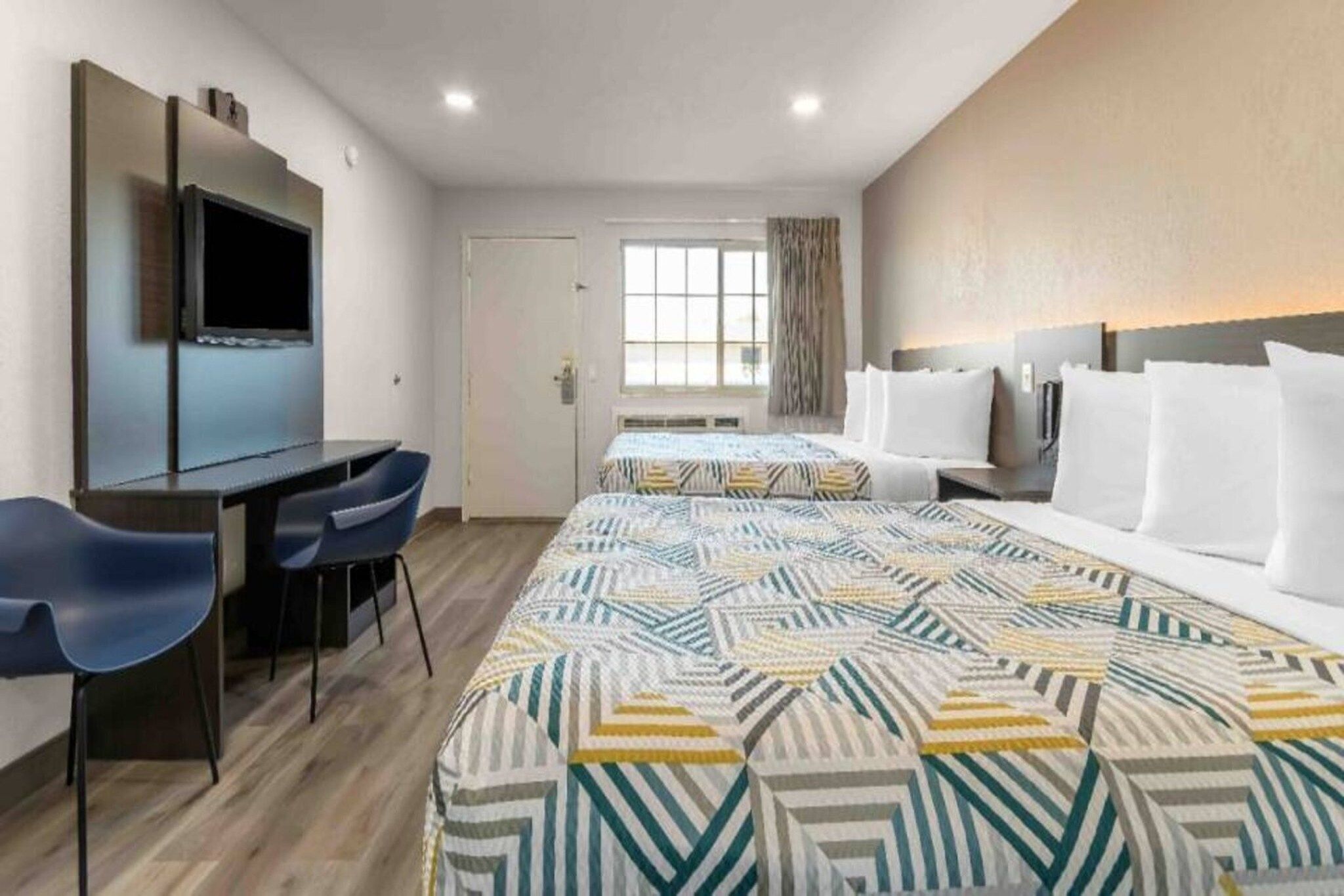 Une chambre d’hôtel avec un lit, un bureau, une chaise, une télévision et une fenêtre.