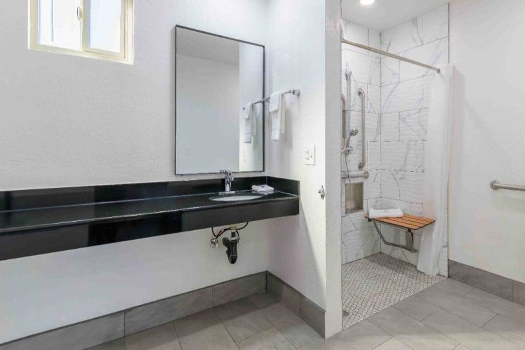 Een badkamer met een zwart aanrechtwastafeltje, een spiegel en een douchegedeelte met een betegelde wand.