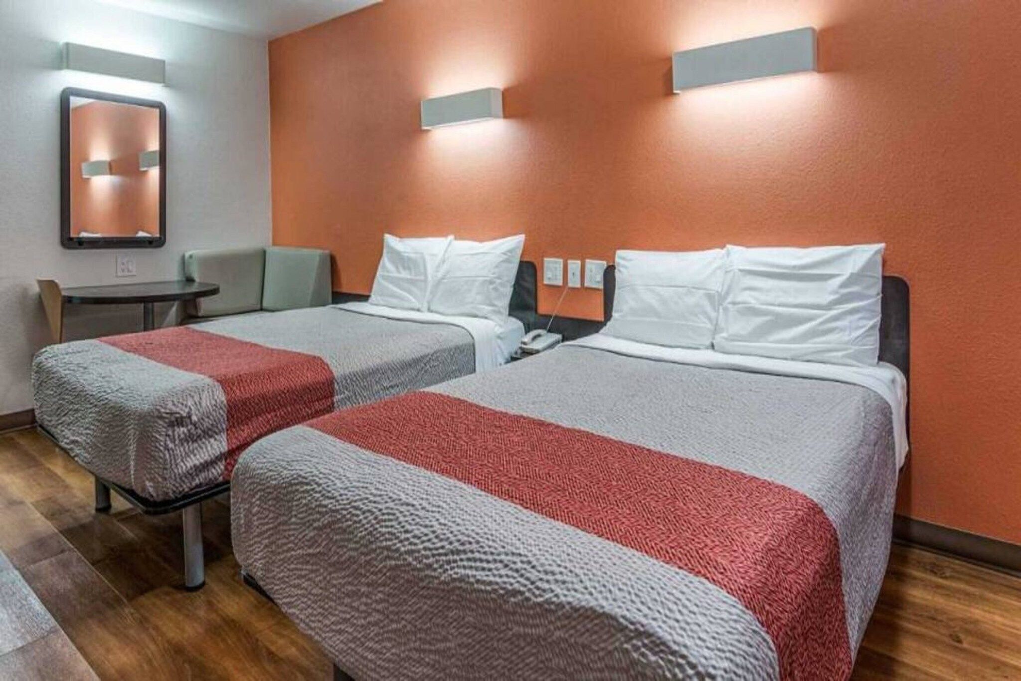 Une chambre d’hôtel avec deux lits, chacun recouvert d’une couverture rouge et grise, une petite table et une chaise.