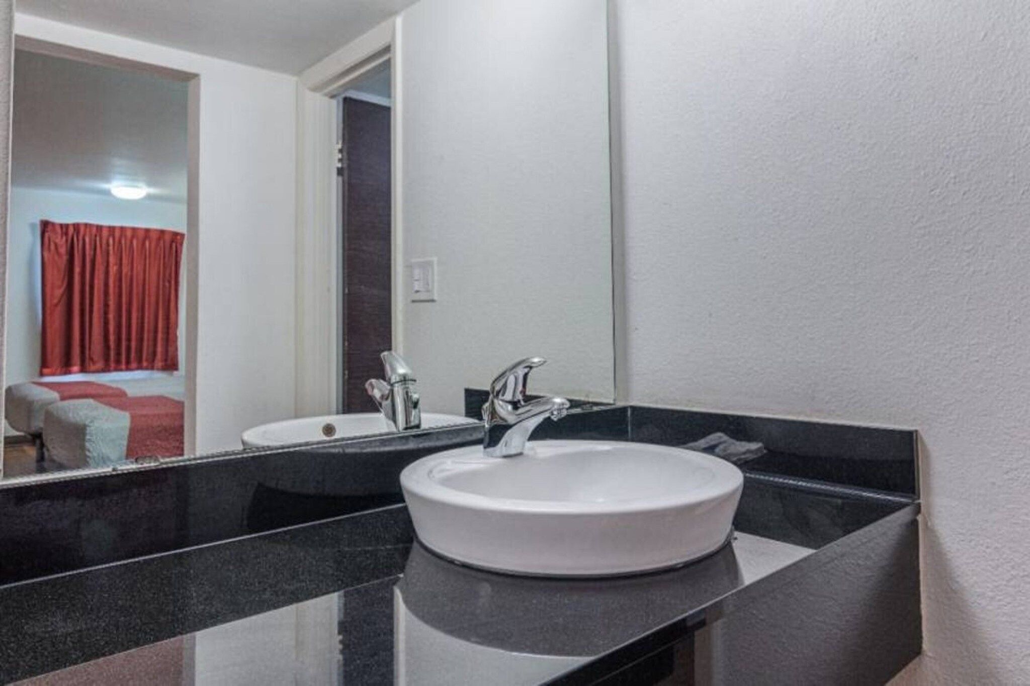 A bathroom with a white sink, a mirror, and a red curtain.