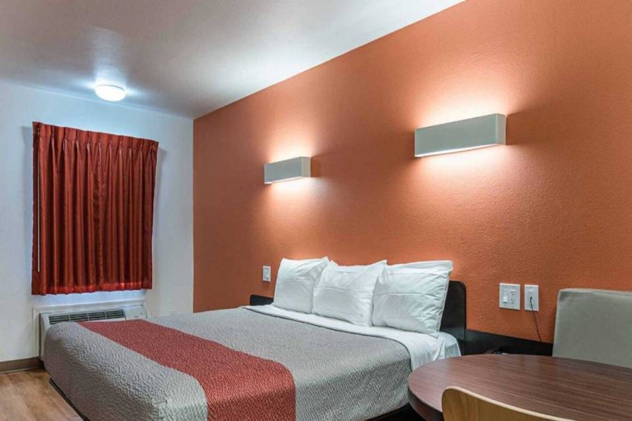 A hotel room with a bed, a table, and a window with curtains.