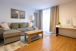 A modern living room with a sectional sofa, a wooden coffee table, and a desk with a chair. - Contemporary 2BDR House with Garden in New Cross (Greater London)