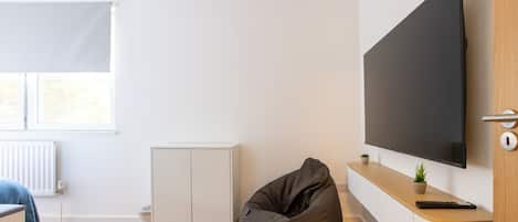 A modern living room with a flat-screen TV, a bean bag chair, a small cabinet, and a radiator.