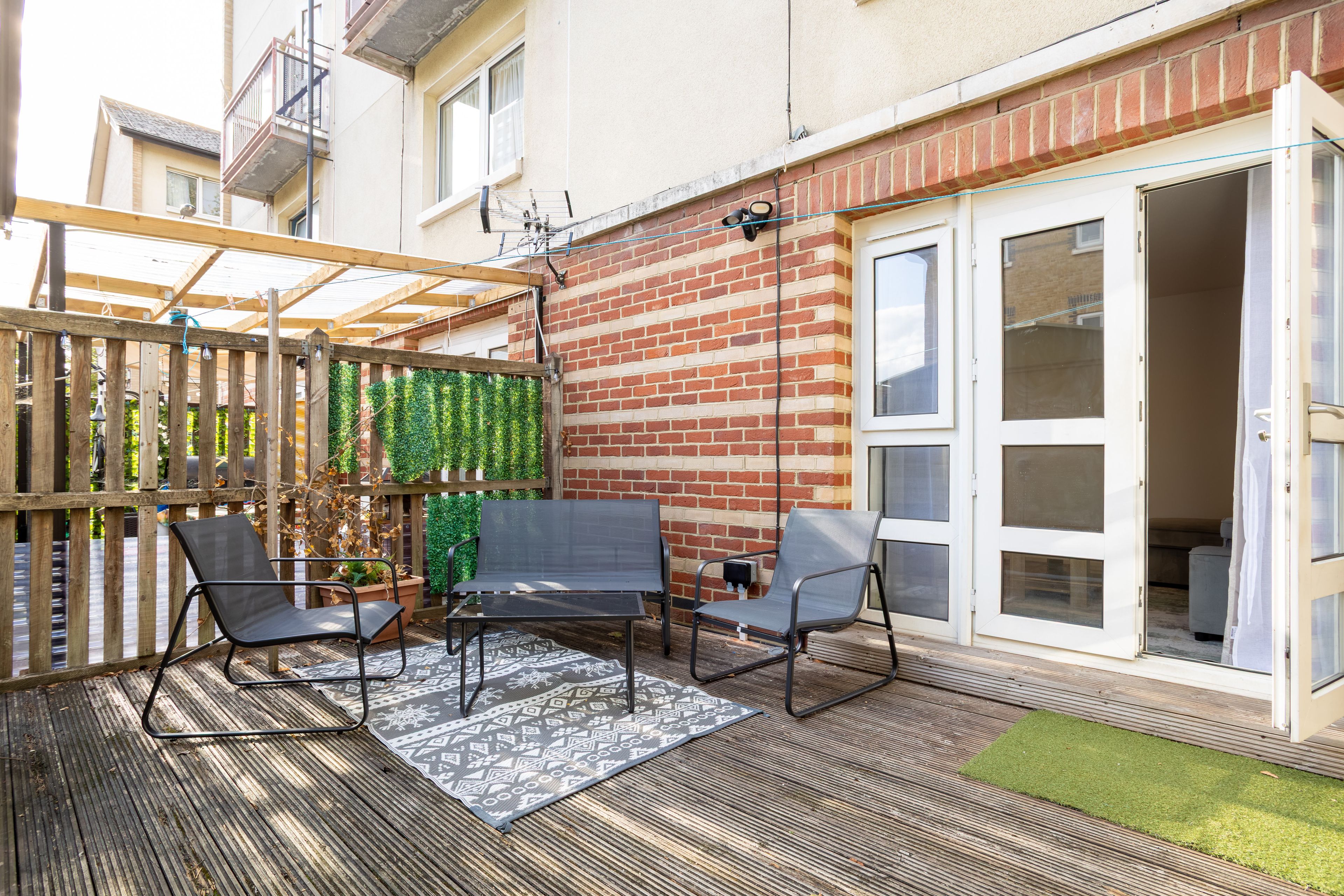 Een terras met een houten omheining, een bakstenen muur en een schuifpui.