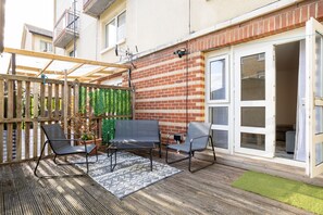 A patio with a wooden fence, a brick wall, and a sliding glass door. - Contemporary 2BDR House with Garden in New Cross (Greater London)