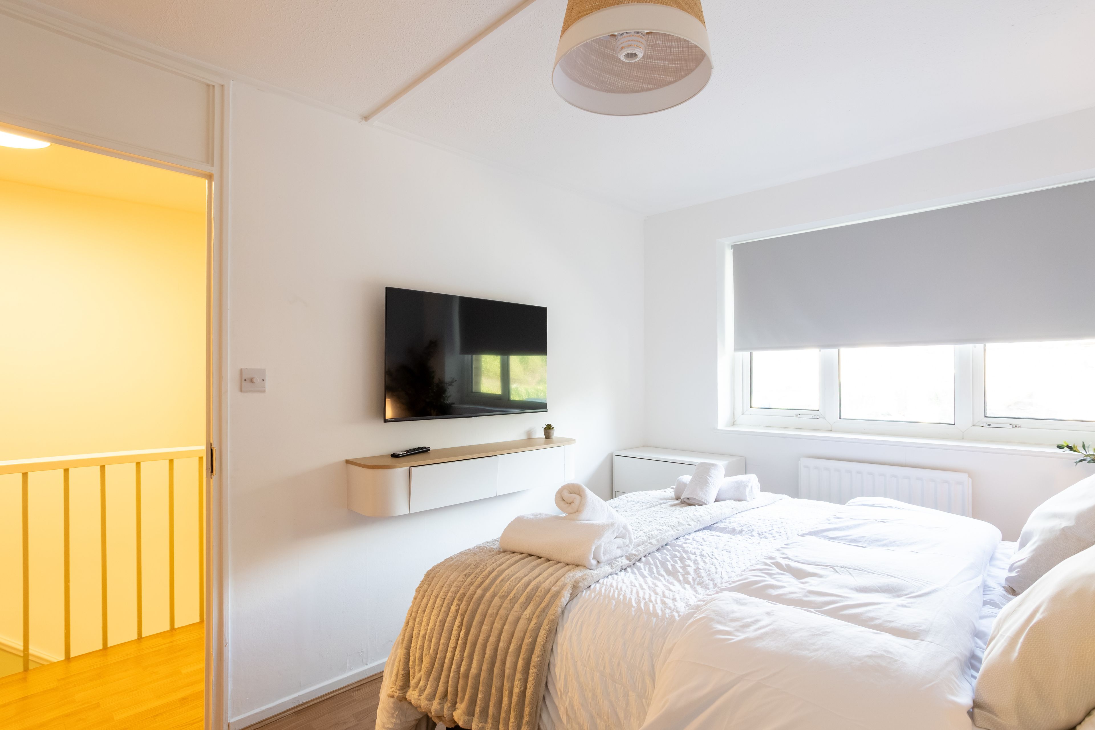 Une chambre moderne avec un lit, un téléviseur fixé au mur, une fenêtre avec un store et un plancher en bois.