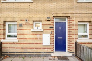 A brick building with a blue door marked with the number 96, windows, and a small shelf with a plant. - Contemporary 2BDR House with Garden in New Cross (Greater London)