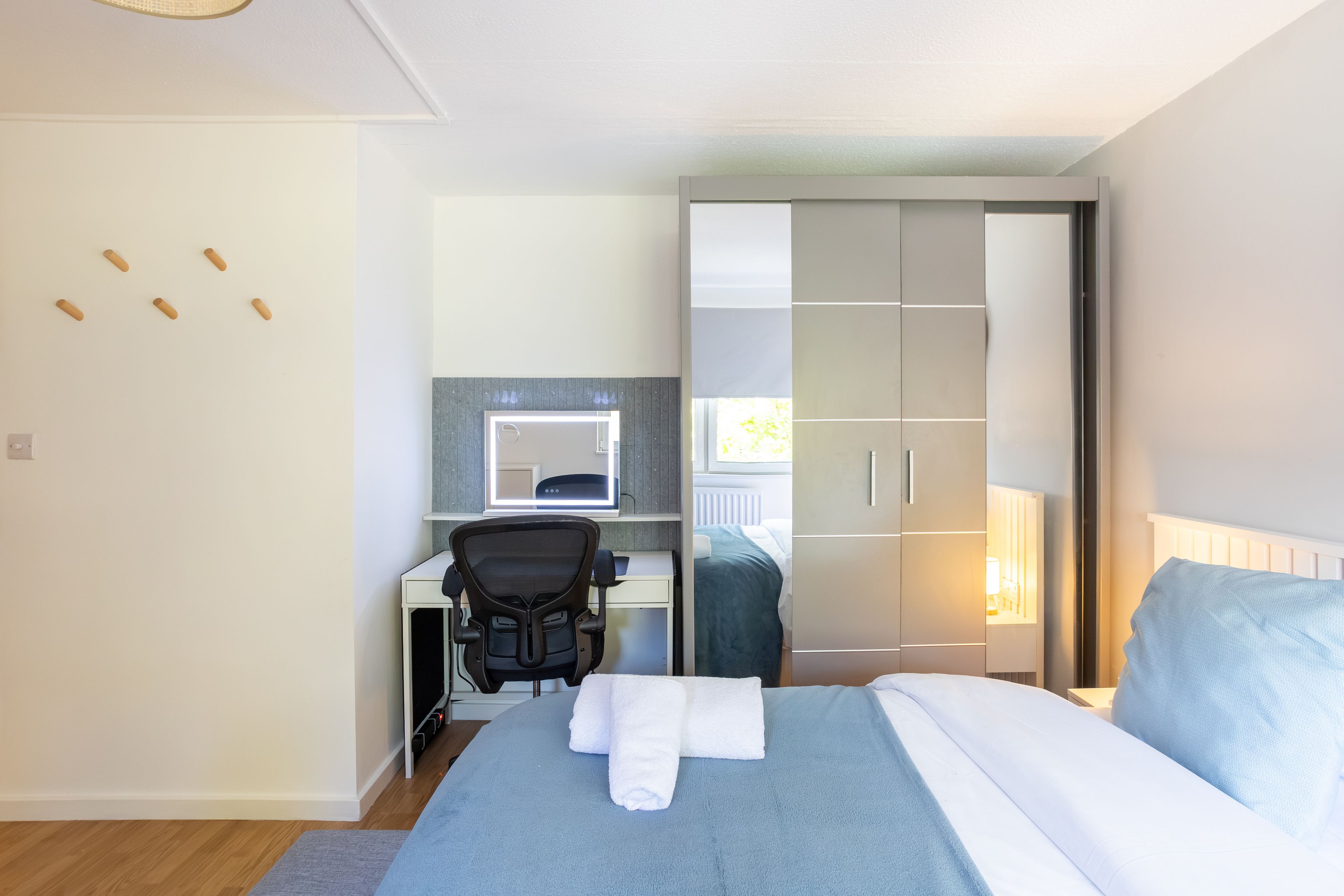 A bedroom with a bed, a desk with a chair, a wardrobe, and a mirror.