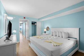 A bedroom with a bed, bedside tables, a TV, and a walk-in closet. - Deluxe Oceanfront Suite | King Bed (Myrtle Beach)