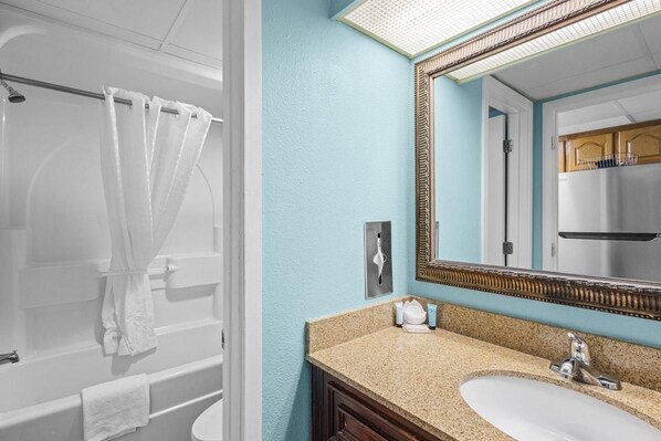 A bathroom with a bathtub, a sink, and a mirror. - Deluxe Oceanfront Suite | King Bed (Myrtle Beach)