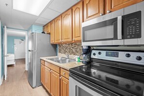A kitchen with wooden cabinets, stainless steel appliances, and a tiled backsplash. - Deluxe Oceanfront Suite | King Bed (Myrtle Beach)