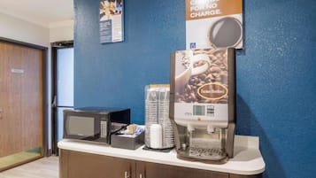 A breakfast bar with a coffee machine, a microwave, and stacked paper cups.