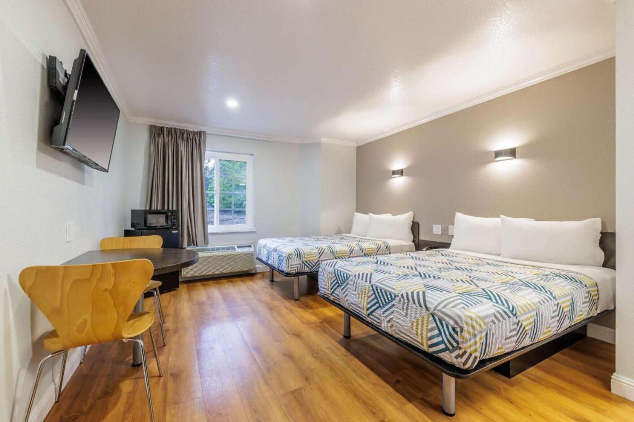 A hotel room with two beds, a desk, a chair, a television, and a window.