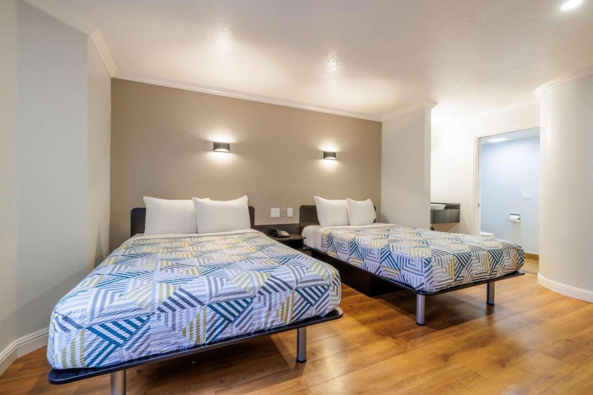 Een hotelkamer met twee bedden, een houten vloer en een deur naar een badkamer.