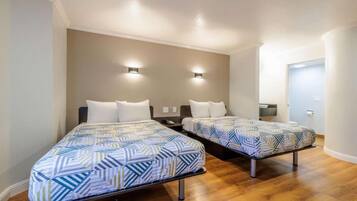 Een hotelkamer met twee bedden, een houten vloer en een deur naar een badkamer.
