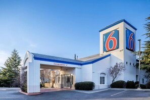 Un motel con un llamativo letrero con el número 6, una entrada despejada y un estacionamiento.