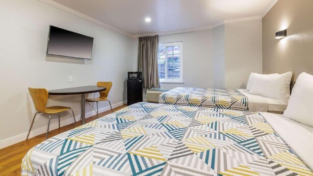 A hotel room with a bed, a desk, a chair, a TV, and a window. - 2 Full Beds | Non-Smoking, Micfridge (Auburn)