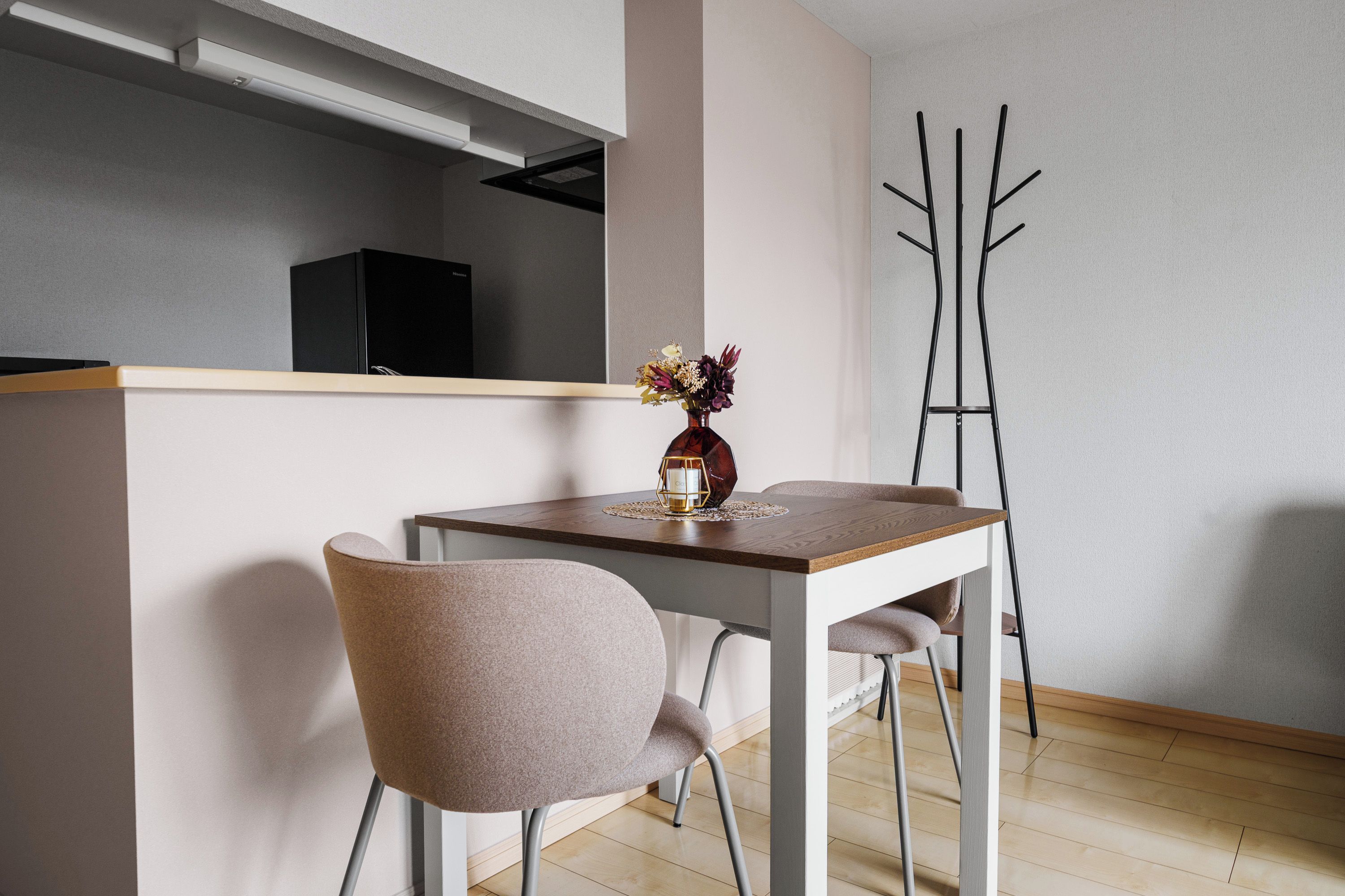 A modern dining area with a table, chairs, a vase with flowers, and a coat rack.