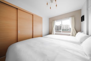 Habitación de hotel con una cama grande, un armario, una ventana con cortinas e iluminación en el techo.