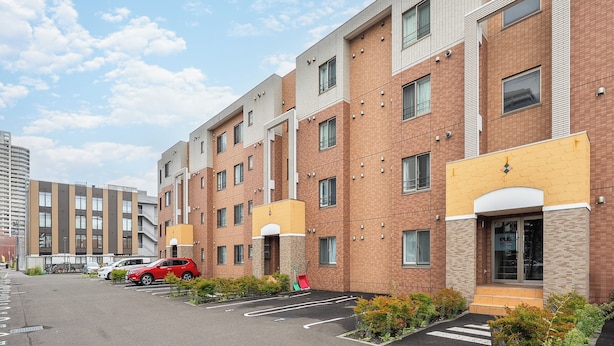 A multi-story residential building with a parking lot in front. - E-US Naebo Station 407 (Sapporo)