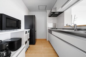 Una cocina moderna con armarios blancos, un refrigerador negro, microondas y cafetera.