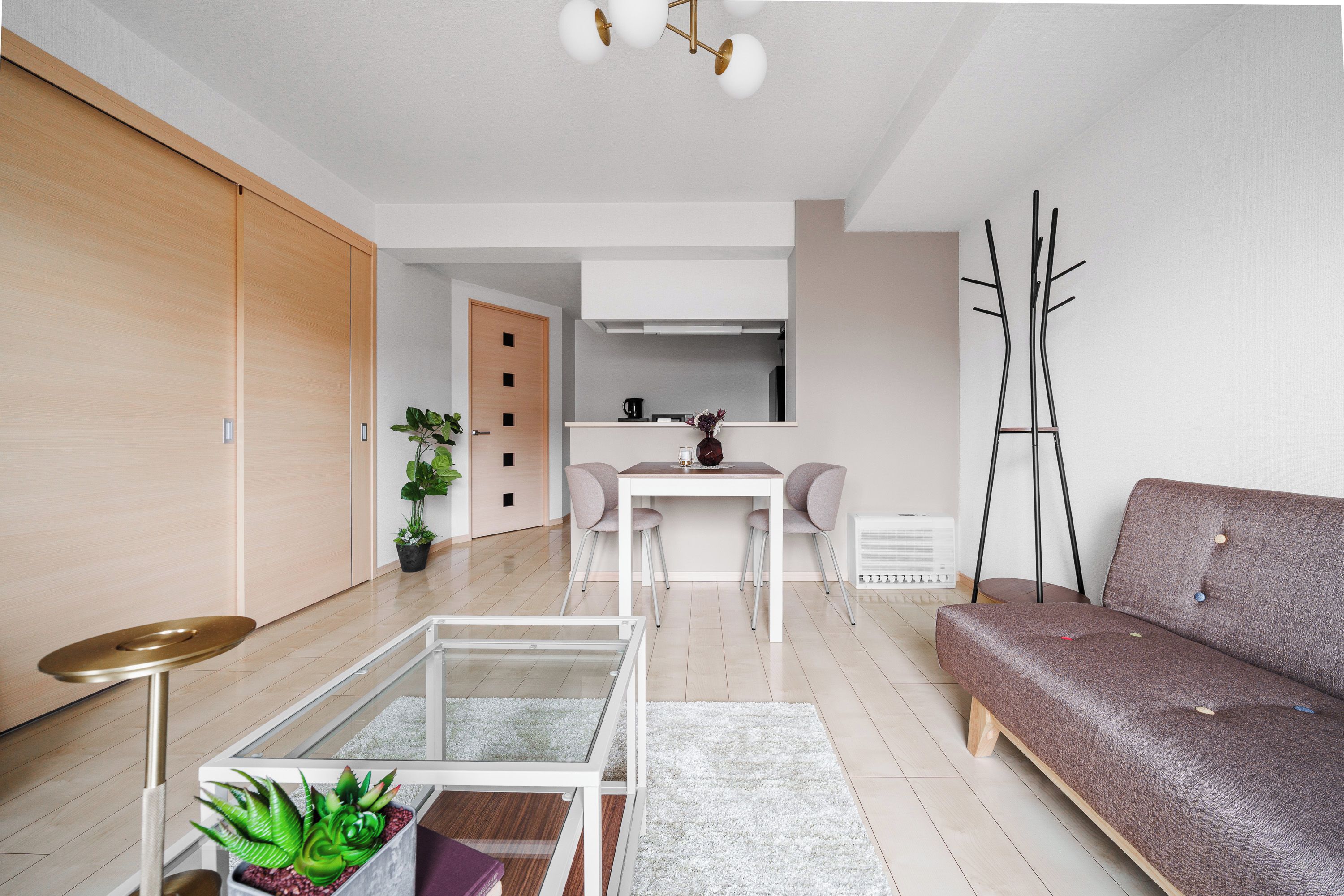 Una sala de estar moderna con un sofá, una mesa de comedor con sillas, una zona de cocina y un perchero.