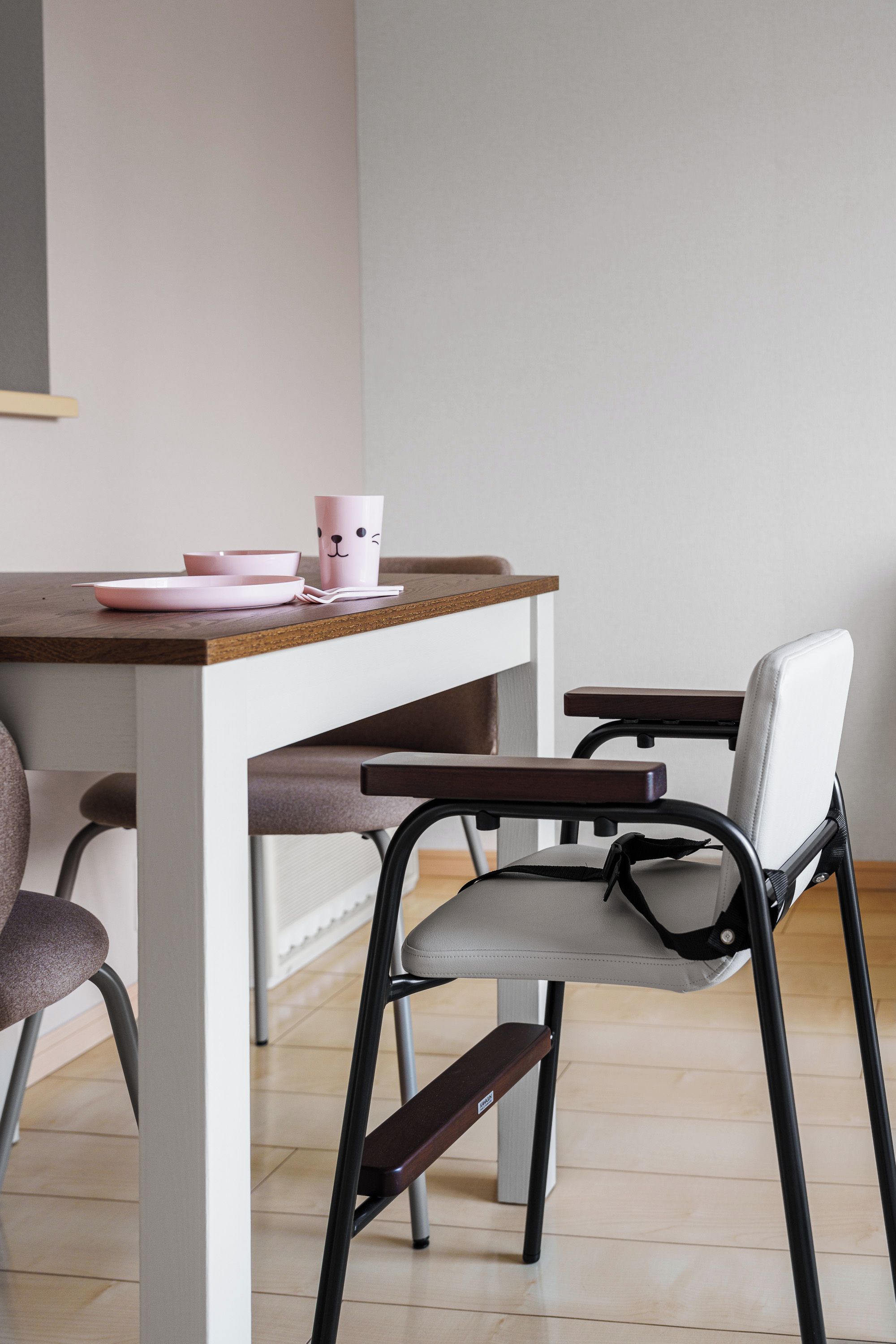 Un comedor con una mesa de madera, una silla con asiento gris y una taza rosa con un diseño de rostro.