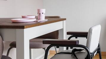 Un comedor con una mesa de madera, una silla con asiento gris y una taza rosa con un diseño de rostro.