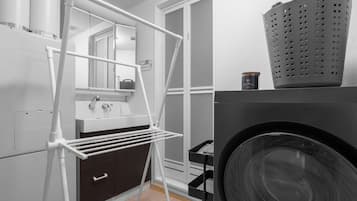 A laundry room with a washing machine, a drying rack, and a small cabinet.