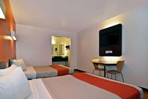 Et hotelværelse med to senge, et skrivebord og et fjernsyn.