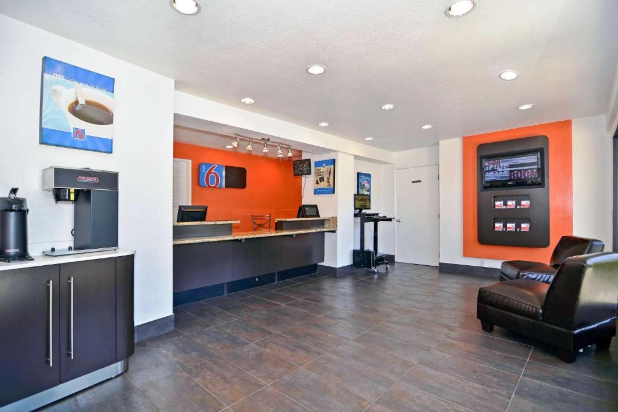 A hotel reception area with a coffee machine, a counter, and a seating area with a chair.