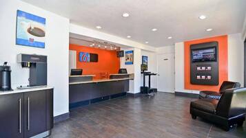 A hotel reception area with a coffee machine, a counter, and a seating area with a chair.