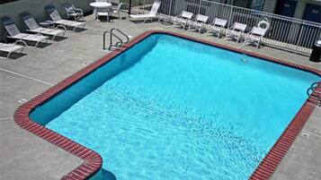 Piscina retangular com borda vermelha, rodeada por espreguiçadeiras brancas e uma pequena mesa.