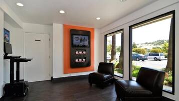 Un área de recepción con un televisor de pantalla plana montado en la pared, una sala de estar con dos sillones, y un ventanal con vistas al estacionamiento y al paisaje.
