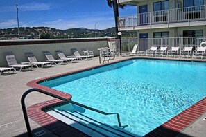 A swimming pool with a red border, surrounded by lounge chairs and a building with a balcony in the background.