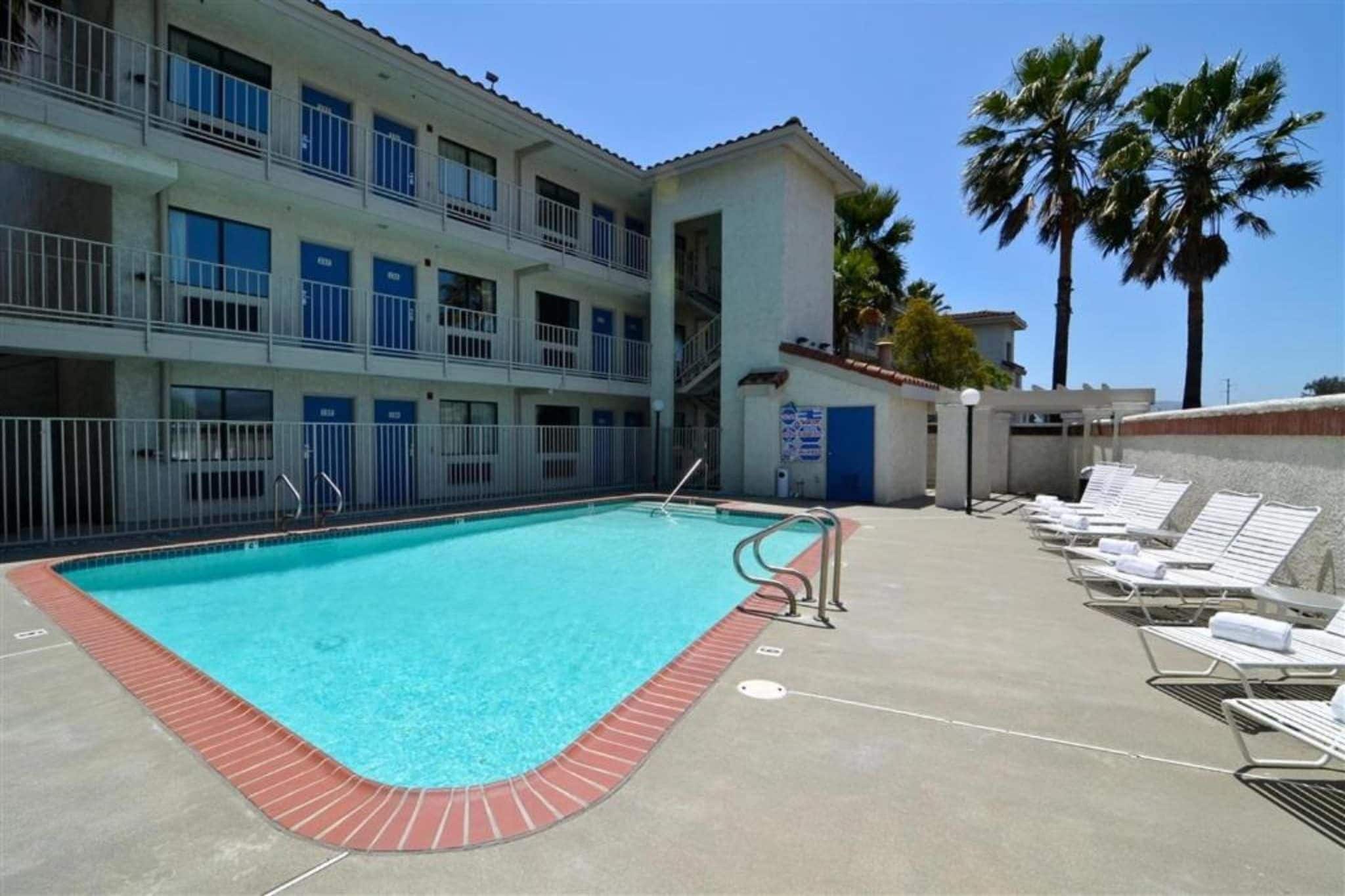 Une piscine bordée de rouge, située à côté d’un immeuble doté de nombreux balcons et d’une porte bleue.