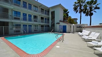 Une piscine bordée de rouge, située à côté d’un immeuble doté de nombreux balcons et d’une porte bleue.
