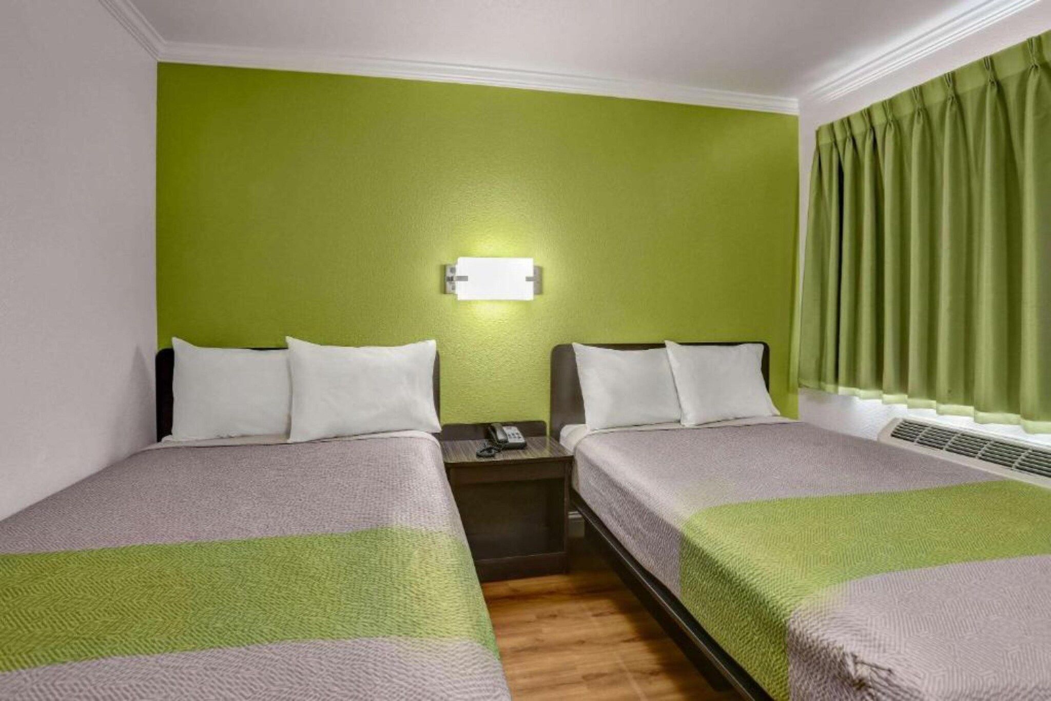 Habitación de hotel con dos camas, una mesita de noche, un teléfono y una lámpara fijada a la pared.